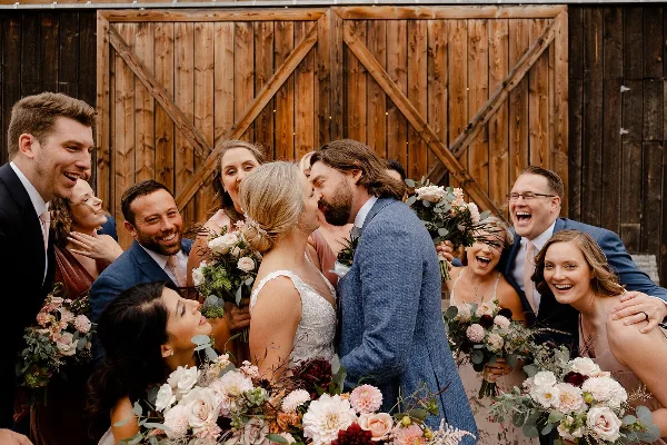 A wedding party posing for a photo in front of a rustic wooden barn door.