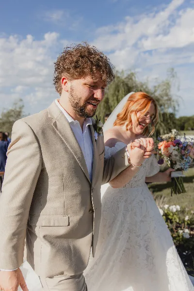 A smiling bride and groom holding hands and walking outdoors during a wedding ceremony.