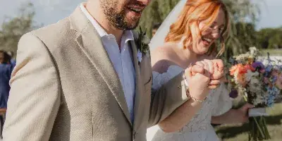 A smiling bride and groom holding hands and walking outdoors during a wedding ceremony.