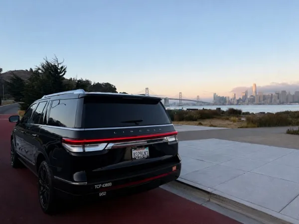Rear view of a black Lincoln SUV with a TCP 4389B decal on the bumper, parked near a waterfront with a city skyline in the background.