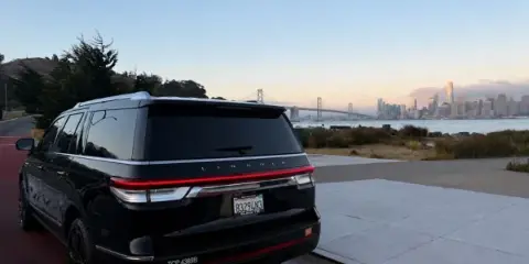 Rear view of a black Lincoln SUV with a TCP 4389B decal on the bumper, parked near a waterfront with a city skyline in the background.