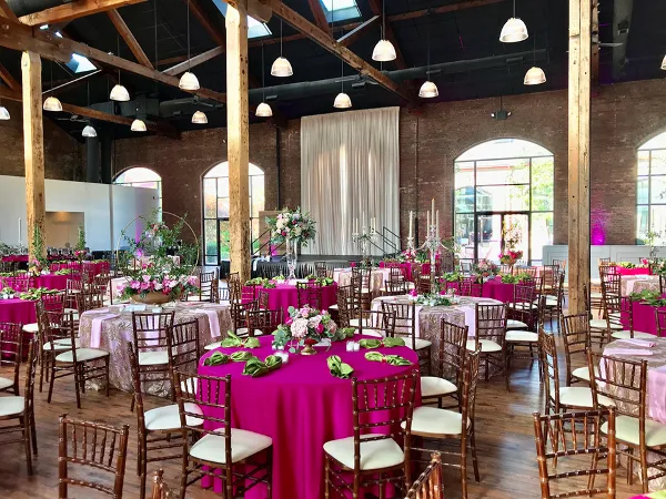 Interior of an industrial-style event venue with exposed brick walls, wooden beams, and tables set for a wedding reception.