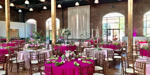 Interior of an industrial-style event venue with exposed brick walls, wooden beams, and tables set for a wedding reception.