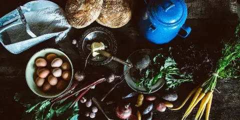 Rustic table setting with loaves of bread, butter, eggs, and fresh vegetables and herbs.