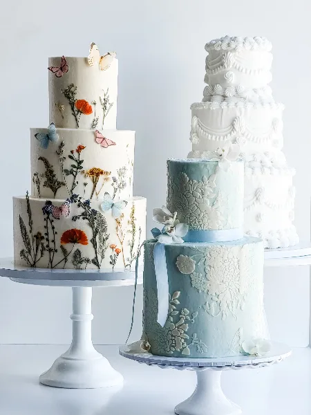 Three multi-tiered wedding cakes with floral and vintage designs displayed on white cake stands.