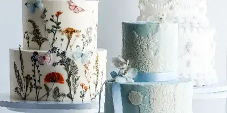 Three multi-tiered wedding cakes with floral and vintage designs displayed on white cake stands.