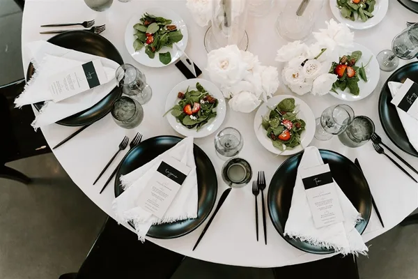 Overhead view of a catering table set with black plates, white napkins, glassware, and small plates of salad.