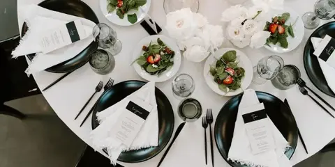 Overhead view of a catering table set with black plates, white napkins, glassware, and small plates of salad.