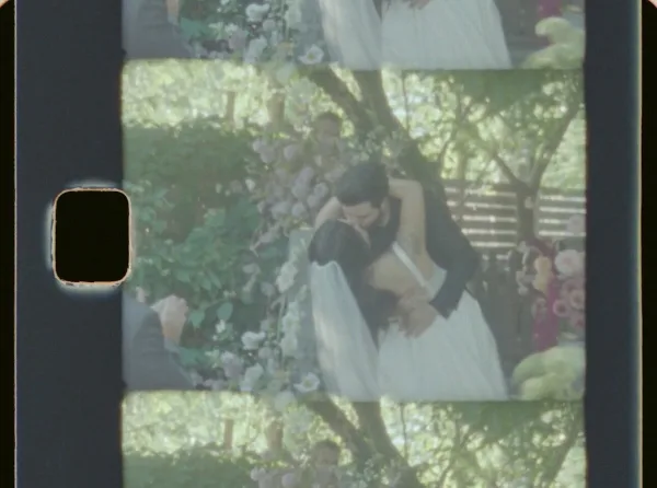 A Super 8 film frame showing a bride and groom embracing at a wedding ceremony.