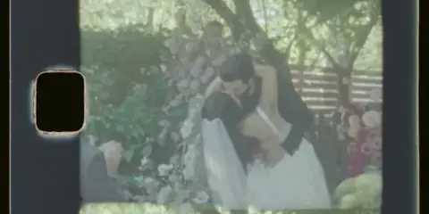 A Super 8 film frame showing a bride and groom embracing at a wedding ceremony.