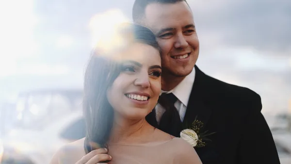 A cinematic close-up of a smiling bride and groom in wedding attire, with a soft lens flare and blurred background.