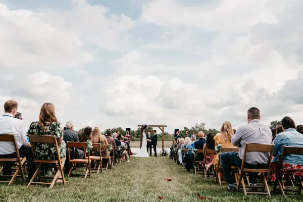 Outdoor wedding ceremony with a bride and groom at an altar and seated guests in a grassy field.