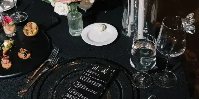 A professionally styled wedding table setting featuring a black tablecloth, floral centerpiece, tall candles, and a custom menu card.