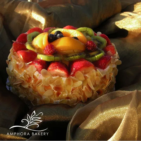 A round cake decorated with sliced strawberries, kiwi, blueberries, and toasted almonds, resting on a gold cloth.