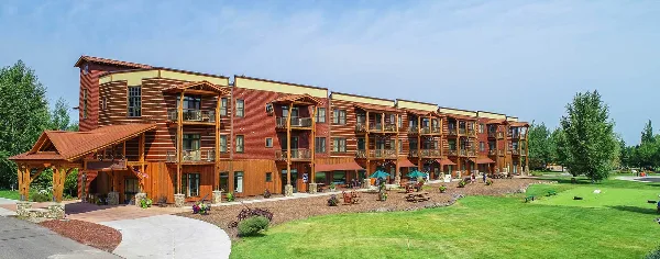 Exterior view of a large, multi-story wooden lodge building with balconies and a manicured lawn.