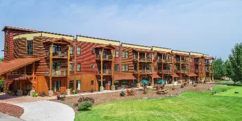 Exterior view of a large, multi-story wooden lodge building with balconies and a manicured lawn.