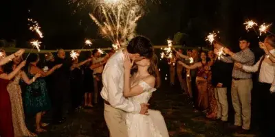 A bride and groom kissing during a sparkler exit at a wedding on a grassy field at night.