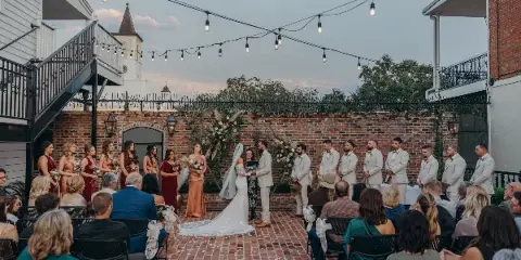 Outdoor wedding ceremony in a brick courtyard with string lights and a floral arch at a historic venue.