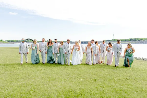 A wedding party standing on a grassy field near a body of water.