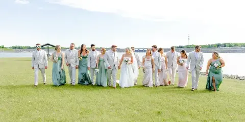A wedding party standing on a grassy field near a body of water.