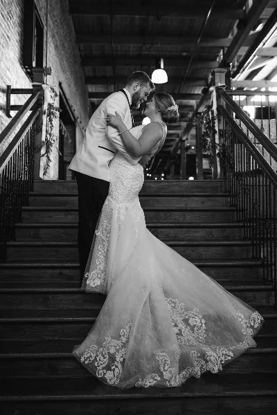 Black and white photograph of a bride and groom embracing on a wooden staircase.