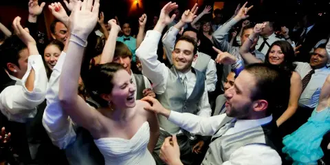 A bride and groom dancing with guests at a wedding reception.