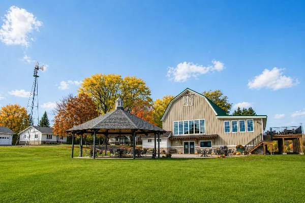 Exterior view of a rustic barn wedding venue with a gazebo, green lawn, and autumn trees.