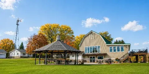Exterior view of a rustic barn wedding venue with a gazebo, green lawn, and autumn trees.