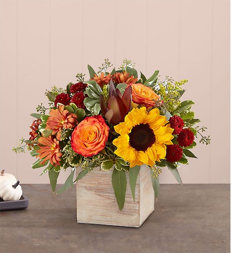 A floral arrangement with sunflowers and orange roses in a wooden box