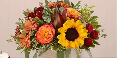 A floral arrangement with sunflowers and orange roses in a wooden box