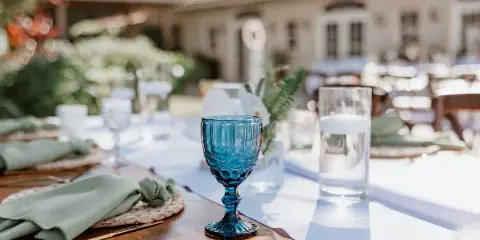 Outdoor event table set with green linens, blue glassware, flatware, and place settings.