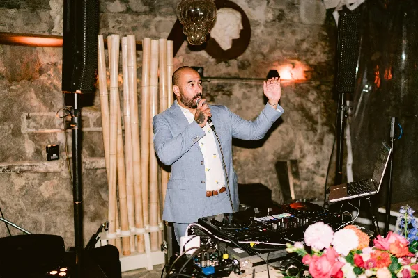 A DJ in a blue suit performing at an event with a microphone and DJ equipment.