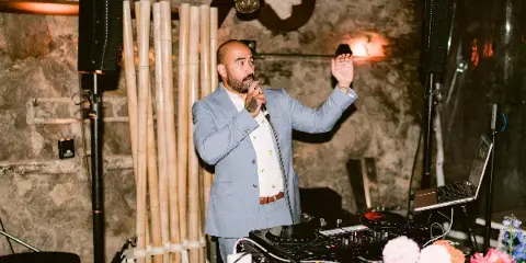 A DJ in a blue suit performing at an event with a microphone and DJ equipment.