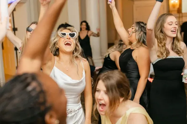 Guests dancing at a wedding reception with raised hands and festive atmosphere.