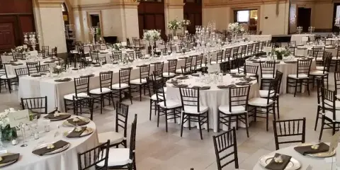 A wedding reception hall set up with round tables, white tablecloths, and crossback chairs.