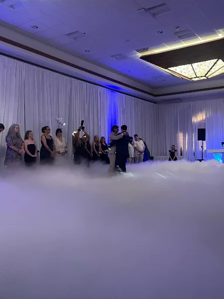 A couple dancing at a wedding reception with low-lying fog effects and blue ambient lighting.