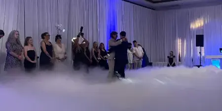 A couple dancing at a wedding reception with low-lying fog effects and blue ambient lighting.