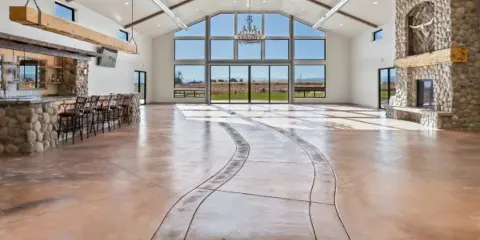 Interior view of a spacious wedding venue with a vaulted ceiling, stone fireplace, bar area, and large windows overlooking a field.