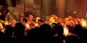 A crowd of people at a party or event with hands raised, illuminated by warm stage lighting.