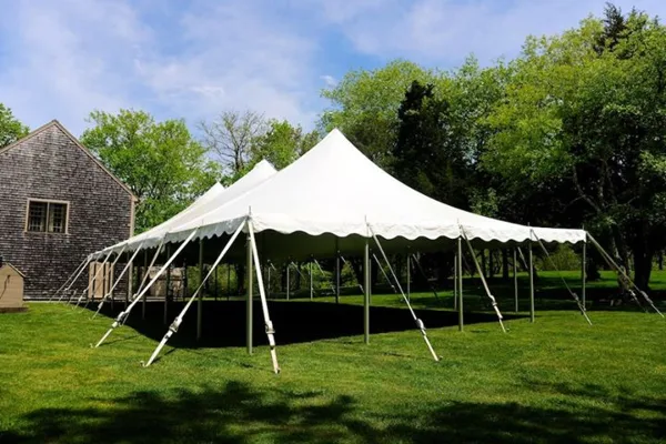 A large white event tent set up on a green lawn with a building and trees in the background.