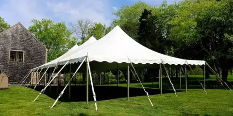A large white event tent set up on a green lawn with a building and trees in the background.