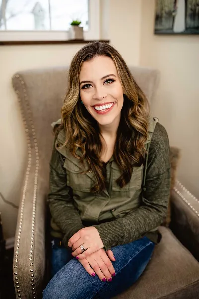 Portrait of Krysta Klinzmann, a cosmetologist, sitting in a chair and smiling.