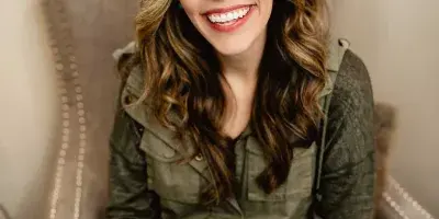 Portrait of Krysta Klinzmann, a cosmetologist, sitting in a chair and smiling.
