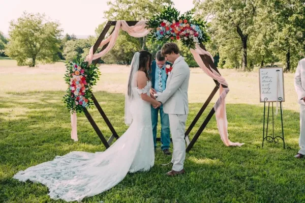 A bride and groom exchanging vows under a floral arch during an outdoor wedding ceremony.