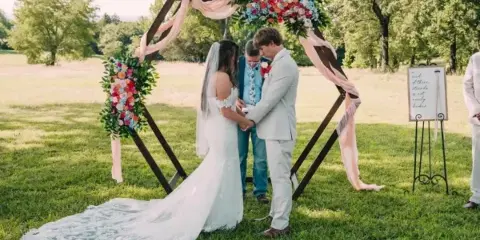 A bride and groom exchanging vows under a floral arch during an outdoor wedding ceremony.