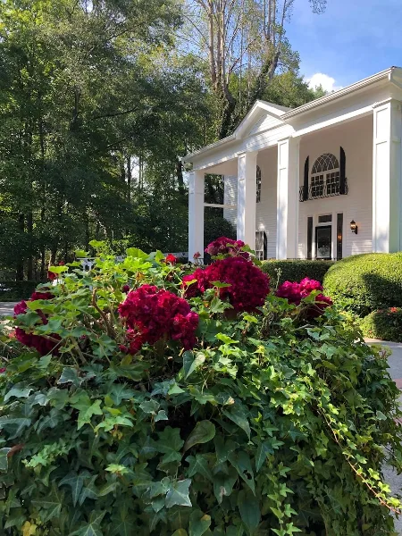 Exterior view of a white wedding venue building with columns and a garden of red flowers in the foreground.