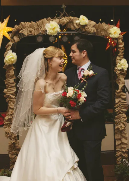 A bride and groom standing together in front of a decorated wedding arch with burlap and flowers.