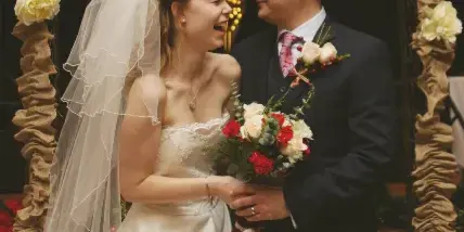 A bride and groom standing together in front of a decorated wedding arch with burlap and flowers.