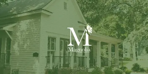Exterior view of a white historic house with a front porch and surrounding garden, branded as Magnolia House and Garden.