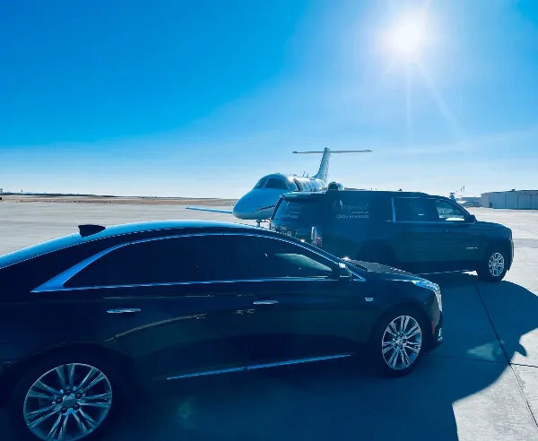 A black sedan and a black SUV with 'Elegance' branding parked on an airport tarmac in front of a private jet.